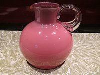 Front view of the pink Polish glass pitcher showing the rounded body and clear handle, highlighting the glossy finish and spout shape.