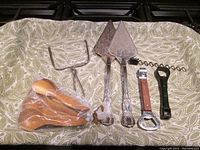 Photo of all serving and bar utensils arranged on patterned cloth including teak spoons in plastic bag, metal utensils, corkscrew and bottle openers