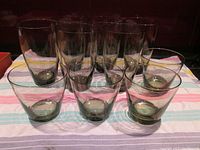 Front view of all 10 smoky drinking glasses arranged on striped cloth, showing both tall and short sizes
