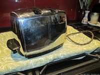 Side view of vintage chrome toaster on patterned cloth, showing reflective metal surface and black lever