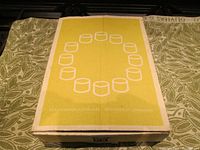 Closed original box with yellow graphic showing 12 linked votive holders in a circular pattern, labeled IKEA PS Varmeljushallare design by Ehlén Johansson.