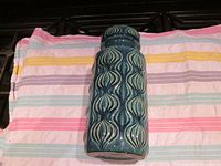 Full side view showing the blue-green glaze and embossed repeating pattern on the vase.