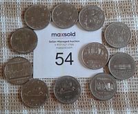 Reverse side of the 11 Canadian nickel dollar coins arranged around auction lot number card showing various commemorative designs and dates.