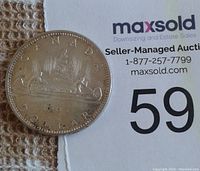 Photo of reverse side of 1965 Canadian silver dollar coin showing voyageur canoe design and inscription.