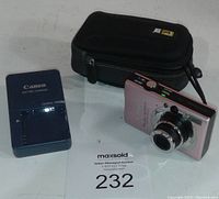 Photo of Canon camera and charger alongside Case Logic carrying case showing front detail of camera lens.