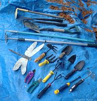 Full view of assorted long-handle and hand gardening tools arranged on blue tarp with some rust and dirt visible