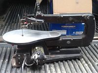 Side view of the Trade Master scroll saw showing its arm, blade, and base with a flexible shaft light attached.