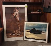 Giraffe plaque and Lawren Harris Pic Island art print side by side in room with wood panel walls.