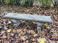 Full view of rectangular concrete bench surrounded by fallen leaves in backyard, showing top surface and legs with decorative detailing.