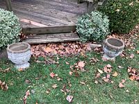 Wide shot showing the pair of concrete planters placed on a grassy area near a wooden deck, surrounded by autumn leaves and shrubs.