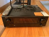 Front view of Denon SLDC receiver with remote and antenna on top, showing main control buttons and LED display