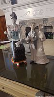 Photo showing one Hollohaza lady figurine and two Lladro wedding couple figurines on a table, capturing front and side views for identification.