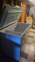Wide angle photo showing the chest freezer with lid open, revealing interior and wire baskets.