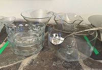 Five clear glass bowls including two Arcoroc France thumbprint serving bowls, a trifle/punch bowl, a plain pedestal bowl, and a small wavy bowl, with two ladles placed on or near the punch bowl.