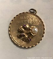 Full front view of circular pendant showing 'Happy Birthday' inscription and central floral motif with purple stones and pearl