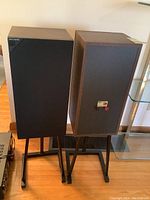Pair of KEF Model C30 speakers shown from front and back angles on black metal stands, wood grain finish sides visible.
