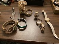 Overview of six ladies watches including a ring watch and various costume watches on a table.