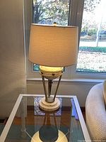 Full view of lamp showing shade and base on glass side table near window.