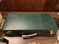 Closed green carrying case for Mah Jongg set with white handle and metal clasps.