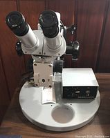 Front view of microscope on round metal base with attached lamp supply box
