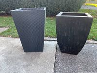 Two outdoor planters side by side on pavement with grass background.