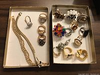Two cardboard trays side by side containing two gold-colored bracelets and about 15 rings in various styles including sterling 925 rings.