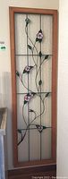 Full view of tall stained glass panel with wood frame, showing entire floral vine design.