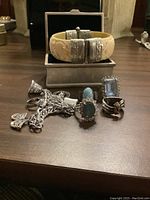 Three sterling silver rings, a silver-colored charm bracelet, and carved bone-colored bracelet inside a metal jewelry box.