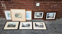Eight framed art prints arranged outdoors showing various coastal and landscape scenes.