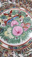 Close-up of Famille Rose decorative plate featuring pink flowers with green leaves and butterflies in border.