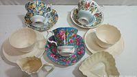 The lot arranged top-down showing three floral Royal Albert cups and matching saucers, three cream-colored trinket dishes, and a Belleek creamer.