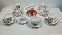 Full set of eleven collectible tea cups and saucers arranged on a white surface, showing various floral patterns and designs.