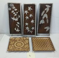 Three rectangular ceramic wall plaques with white botanical designs and two square serving trays with intricate brown patterns shown together.