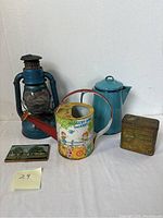Photo showing the full lot of five tin items on white background including the lantern, watering can, coffee pot, cigarette case, and tin box.