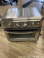 Front view of silver Cuisinart TOA-60C air fryer convection oven with control dials and closed door on wooden floor.