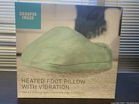 Box front showing product image of the pale green heated foot pillow with vapor branding and feature highlights including heat, 3 intensity levels, and automatic timer.