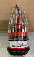 Closed view of the 30+1 screwdriver bit set in cylindrical clear plastic case with red and black base.