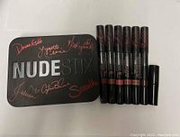 Black metal Nudestix Nude tin with signatures and 6 lip pencils plus sharpener laid out horizontally.