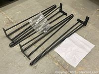 Four black metal hairpin table legs arranged on a flat surface showing mounting plates and rods. One clear plastic bag and assembly instructions included.
