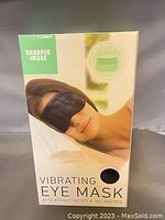 Front of product box showing image of woman wearing the black vibrating eye mask and branding.