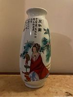 Front view of the vase showing a colorful painted scene of a woman in traditional clothes sitting beside a bird and floral design along with Chinese characters.