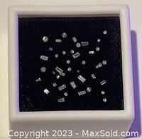 Top view of small mixed cut natural diamonds in a white box with black felt interior, showing round and baguette shapes scattered inside.