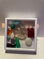 Top-view photo of the gemstone collection in a white-framed glass display case showing various colorful stones.
