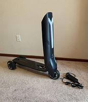 Scooter in folded position on carpet with charger at side