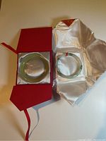 Both jade bangles displayed in red gift box and white satin-lined box.
