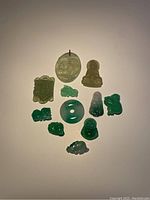 Photo showing all 11 jade pendants arranged on a flat surface, displaying their varied shapes, colors, and carving details.