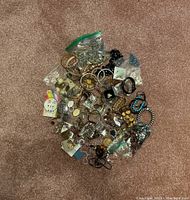 Large pile of assorted jewellery including chains, bracelets, and earrings on a carpet background.
