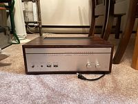 Front view of amplifier showing silver brushed aluminum face, control knobs and attached power cord