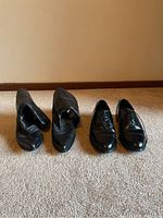 Two pairs of men's black footwear on carpet, one boots and one dress shoes showing outer view