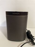 Front view of black Sonos wireless smart speaker with mesh grille and Sonos logo on top front.